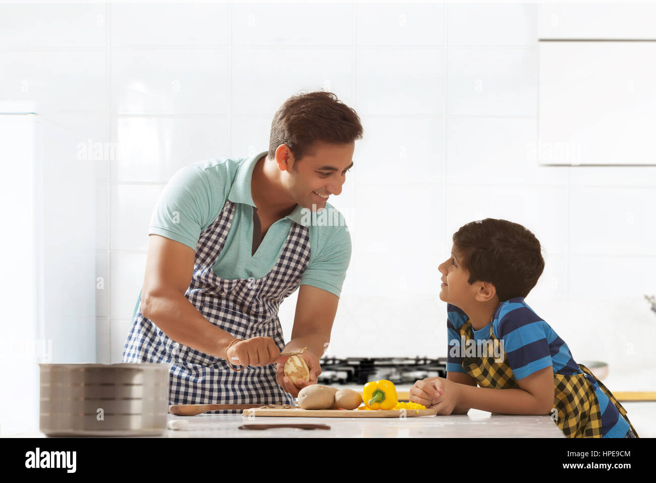 Padre sbucciare le patate in cucina mentre si parla al suo figlio Foto Stock