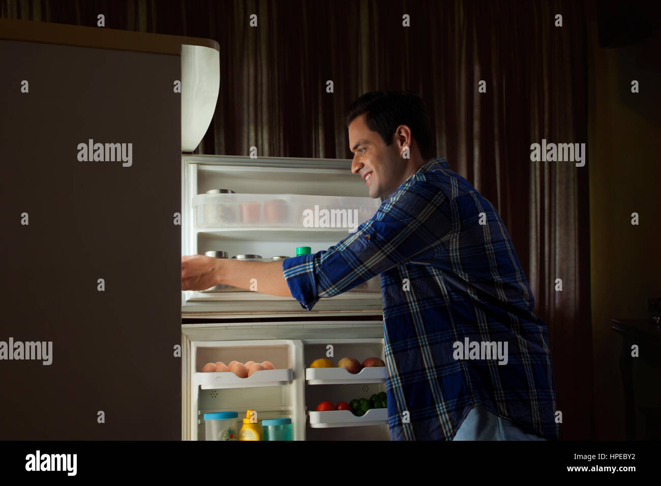 Giovane uomo in piedi in cucina cercando nel frigo Foto Stock