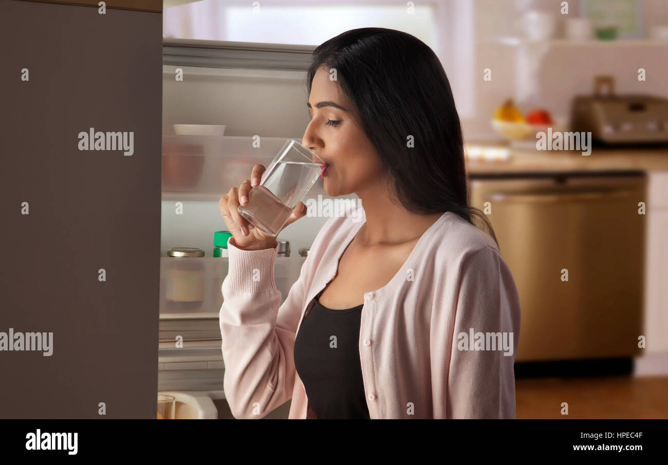 Giovane donna acqua potabile nella parte anteriore del frigorifero aperto Foto Stock