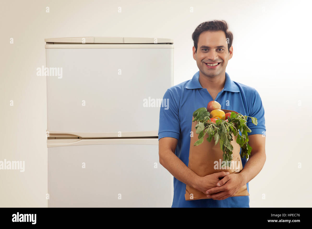 Sorridente giovane azienda sacchetto di frutti in piedi nella parte anteriore del frigorifero Foto Stock