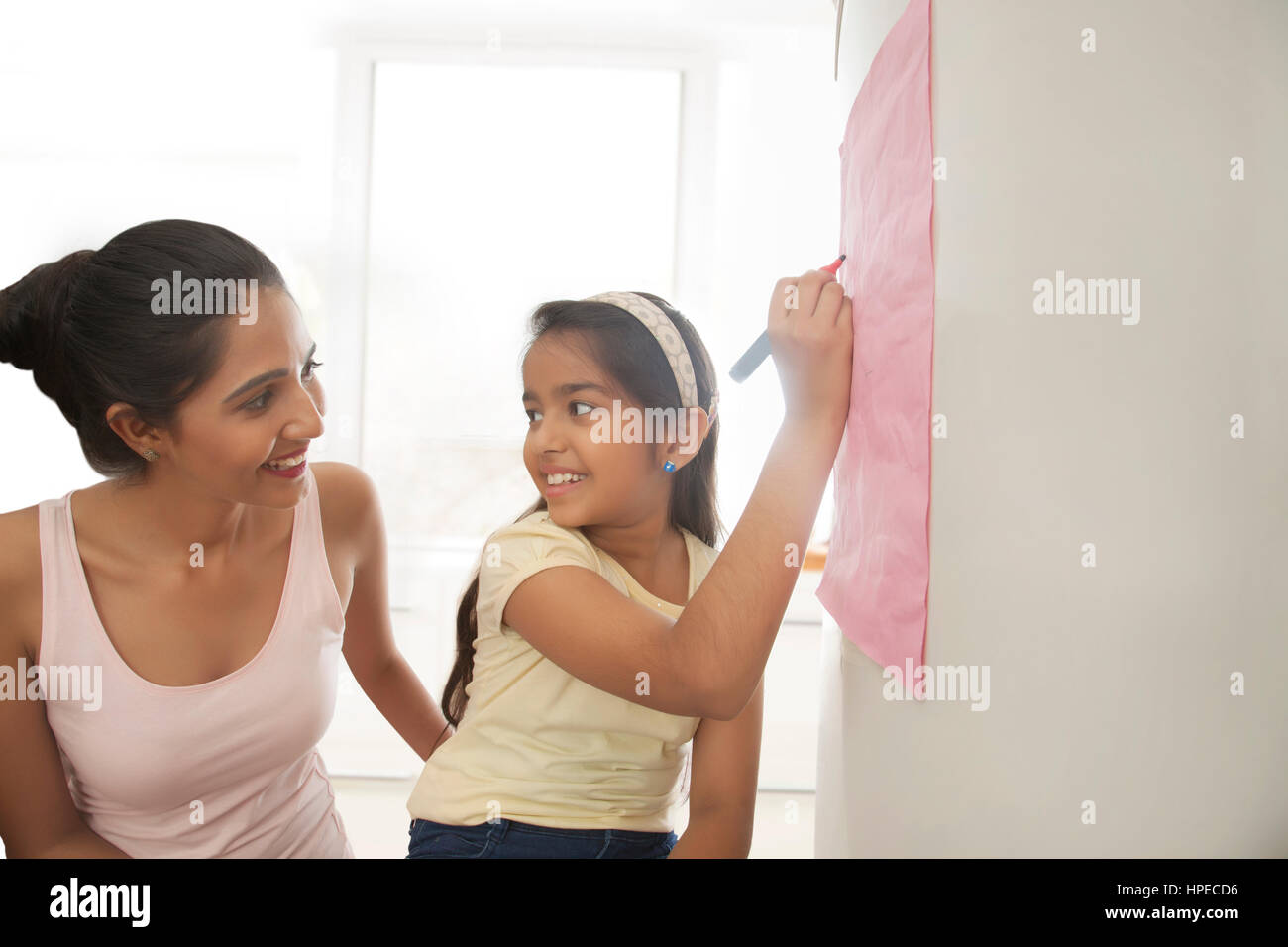 Madre sorridente guardando a sua figlia di scrittura di messaggi sul frigorifero Foto Stock