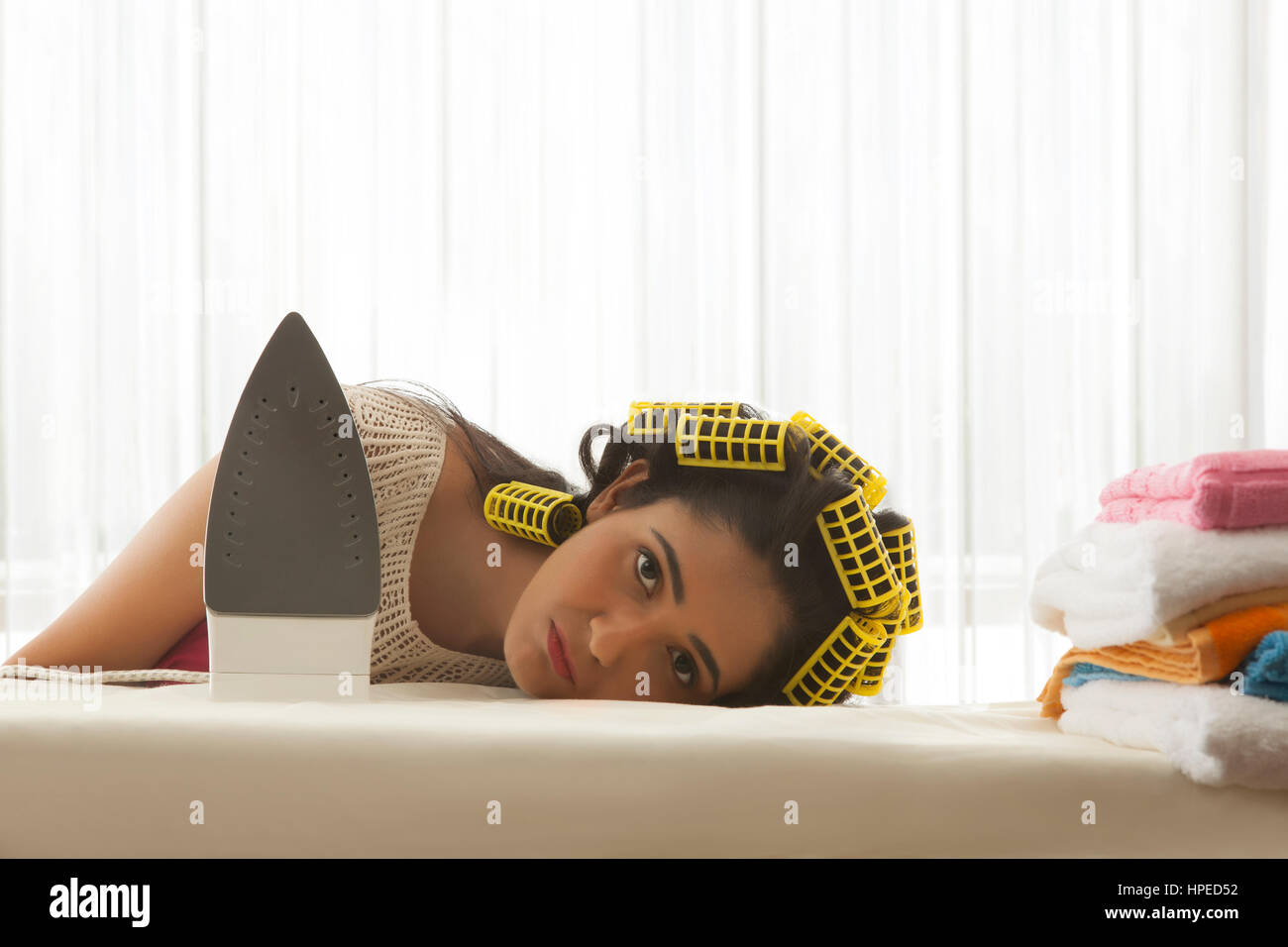 Giovane donna con bigodini dormire a tavola da stiro Foto Stock