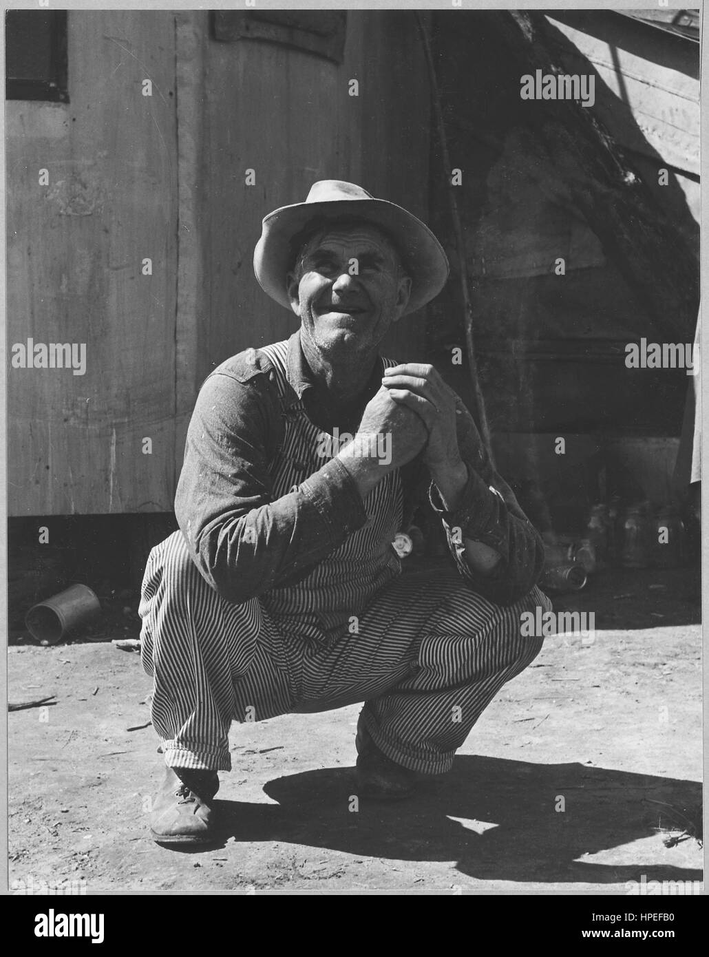 Fotografia di un azienda agricola migrante operaio squatting e sorridente, Olivehurst, California, 20 marzo 1940. Immagine cortesia Dorothea Lange/US National Archives. Foto Stock