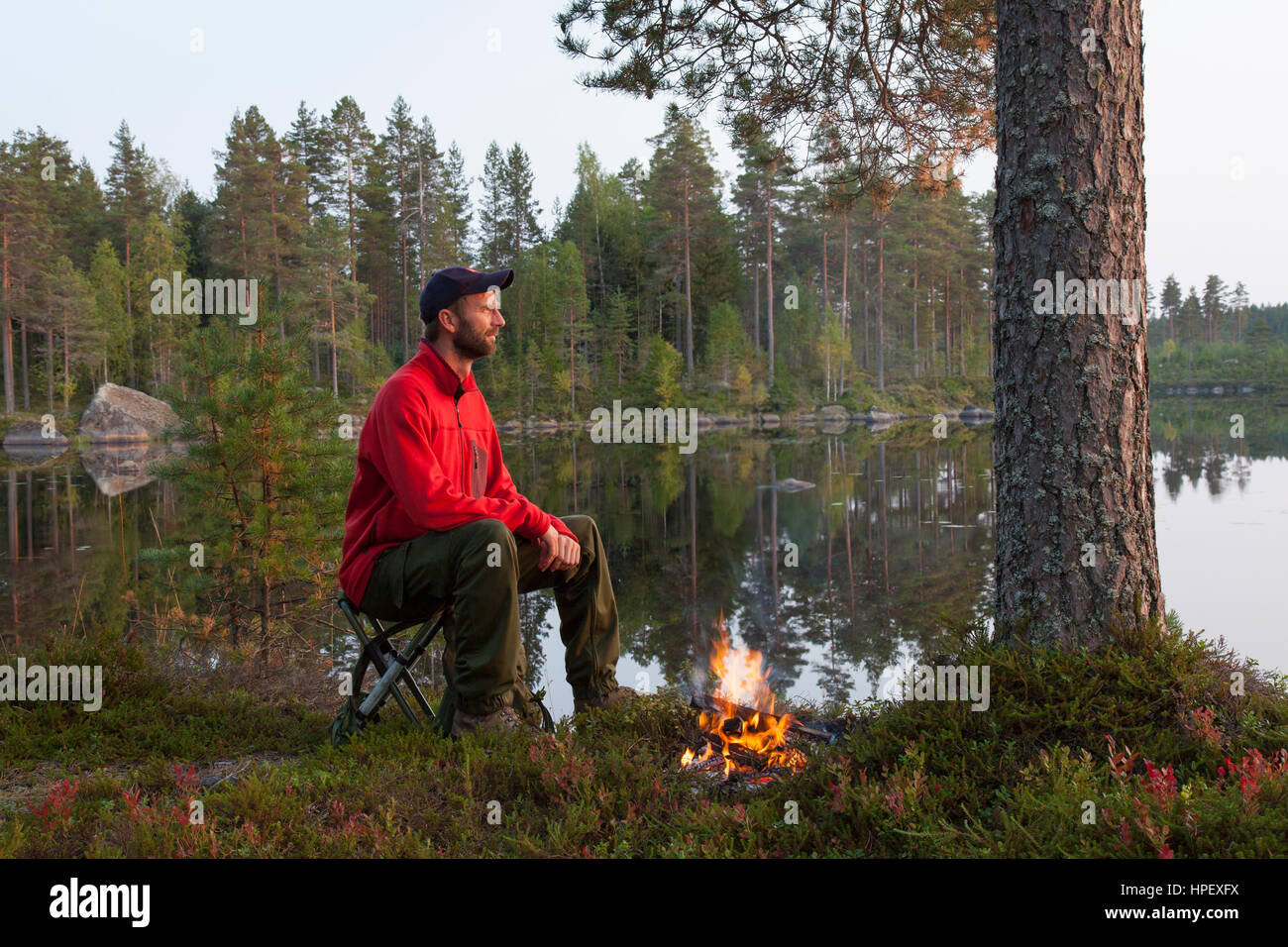 Escursionista acqua bollente nel bollitore di stagno su fuoco di campo mentre il campeggio lungo il lago Foto Stock