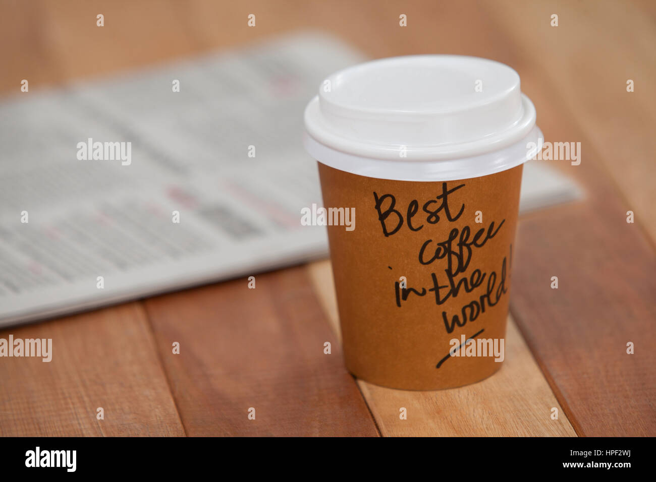 Close-up di monouso per tazza di caffè e un giornale su sfondo di legno Foto Stock