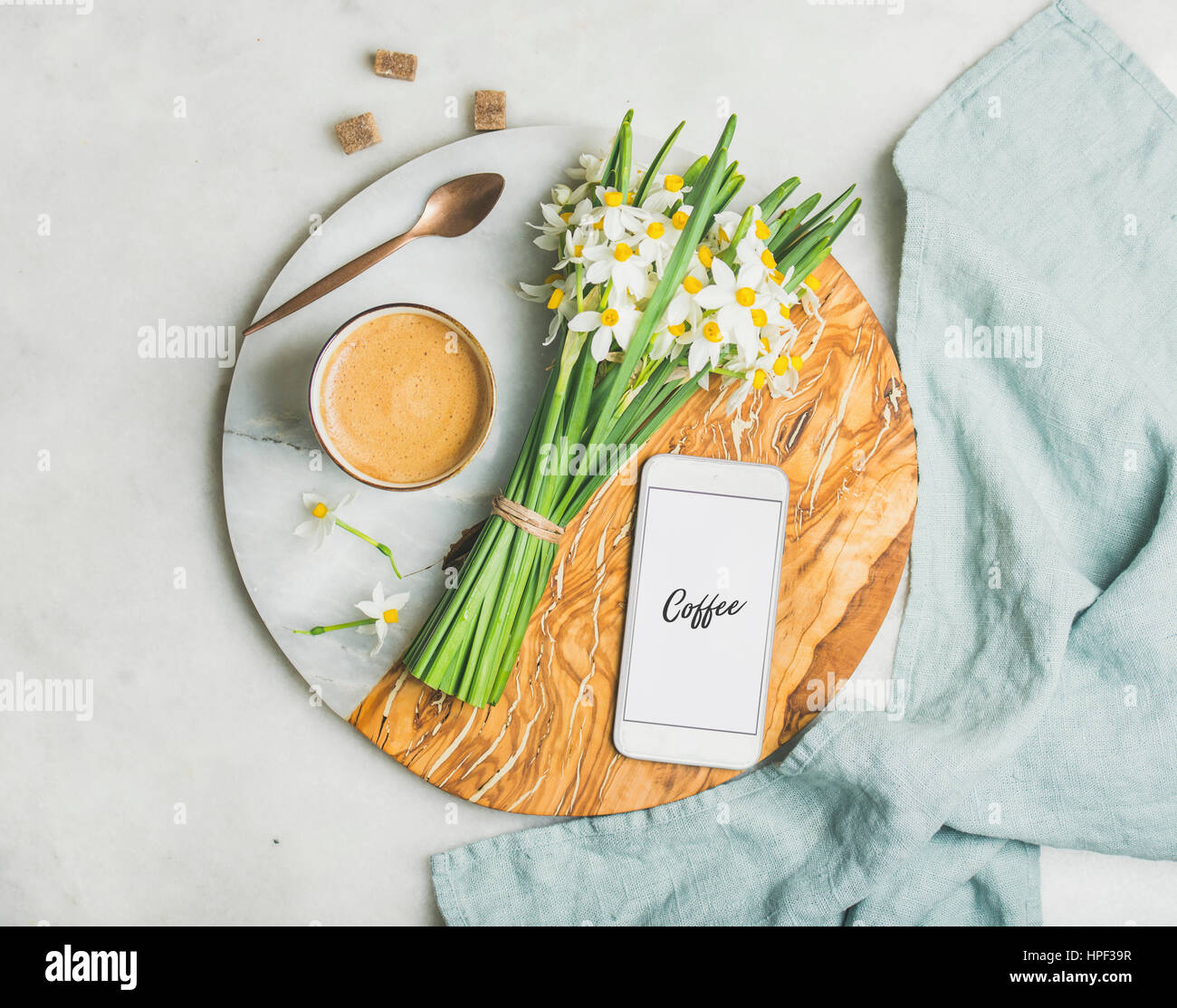 Tazza di caffè del mattino, cucchiaio di fiori di primavera e il telefono cellulare con il testo del caffè sulla scheda Servizio su grigio chiaro sfondo marmo, vista dall'alto. Mornin Foto Stock