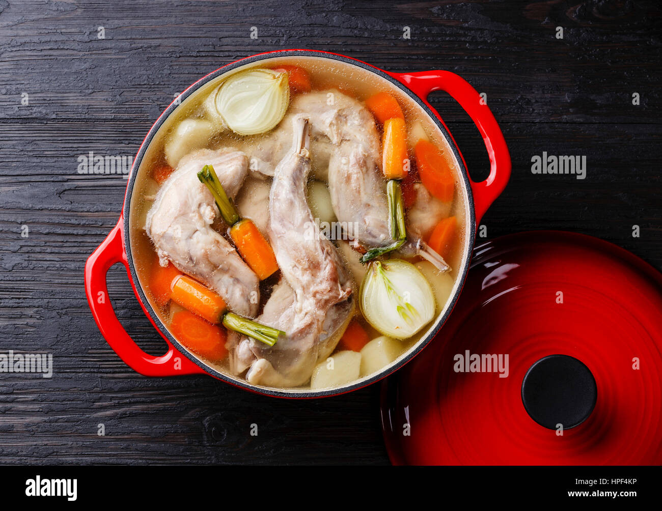 Stufato di coniglio con patate e carote in ghisa pan su nero bruciato sullo sfondo di legno Foto Stock