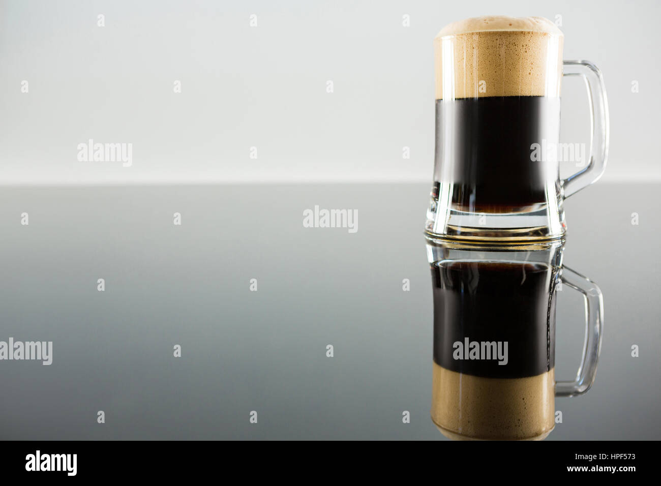 Birra nera in vetro e la sua riflessione sul tavolo Foto Stock