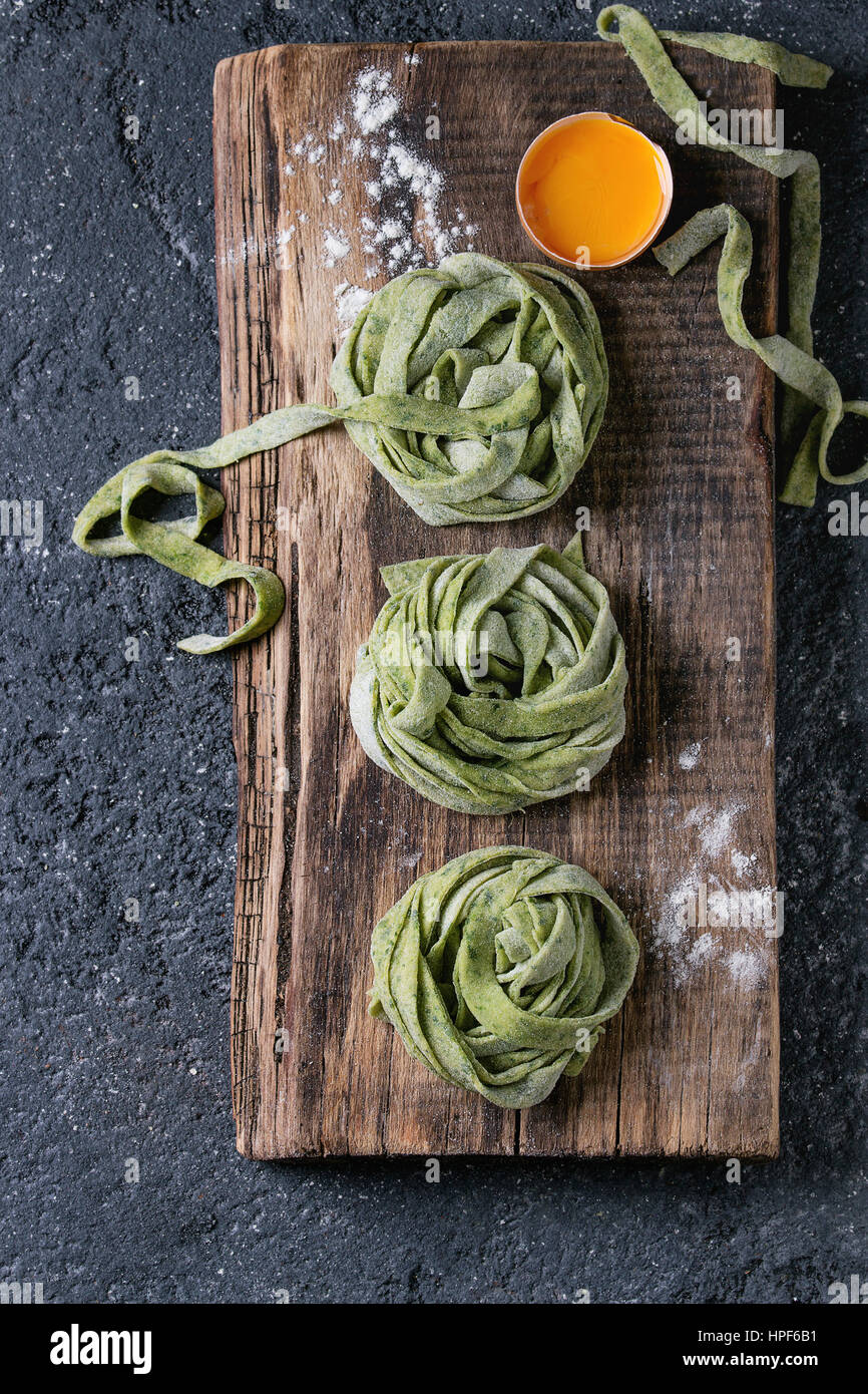 Crudo fresco non cotti in casa verde ritorto spinaci tagliatelle di pasta con il tuorlo d'uovo e farina di legno taglio chopping board su texture scuro concret Foto Stock