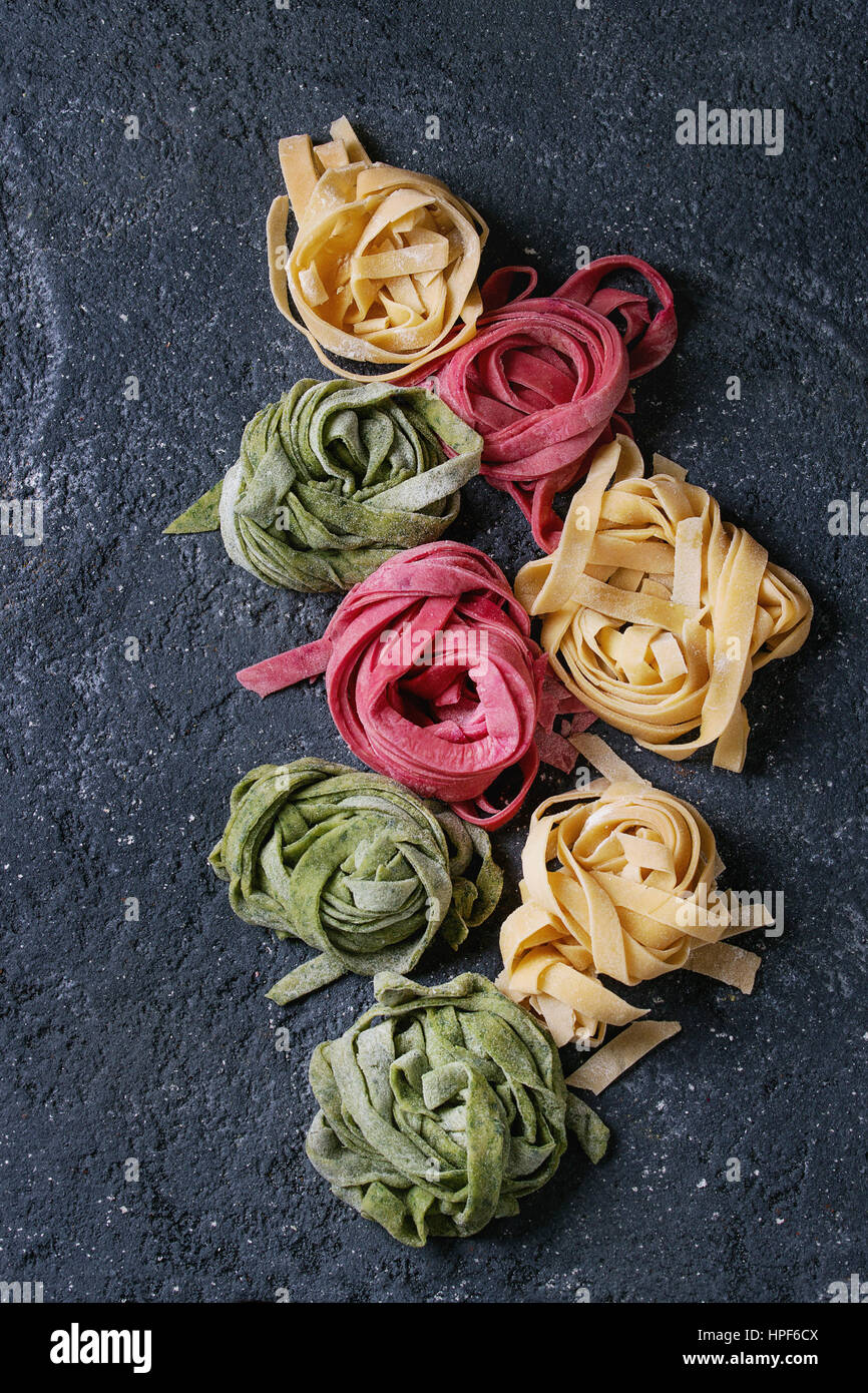 Varietà di colore crudo fresco non cotti pasta fatta in casa tagliatelle spinaci verde, rosa la barbabietola e tradizionale giallo su calcestruzzo scuro dello sfondo. A Foto Stock