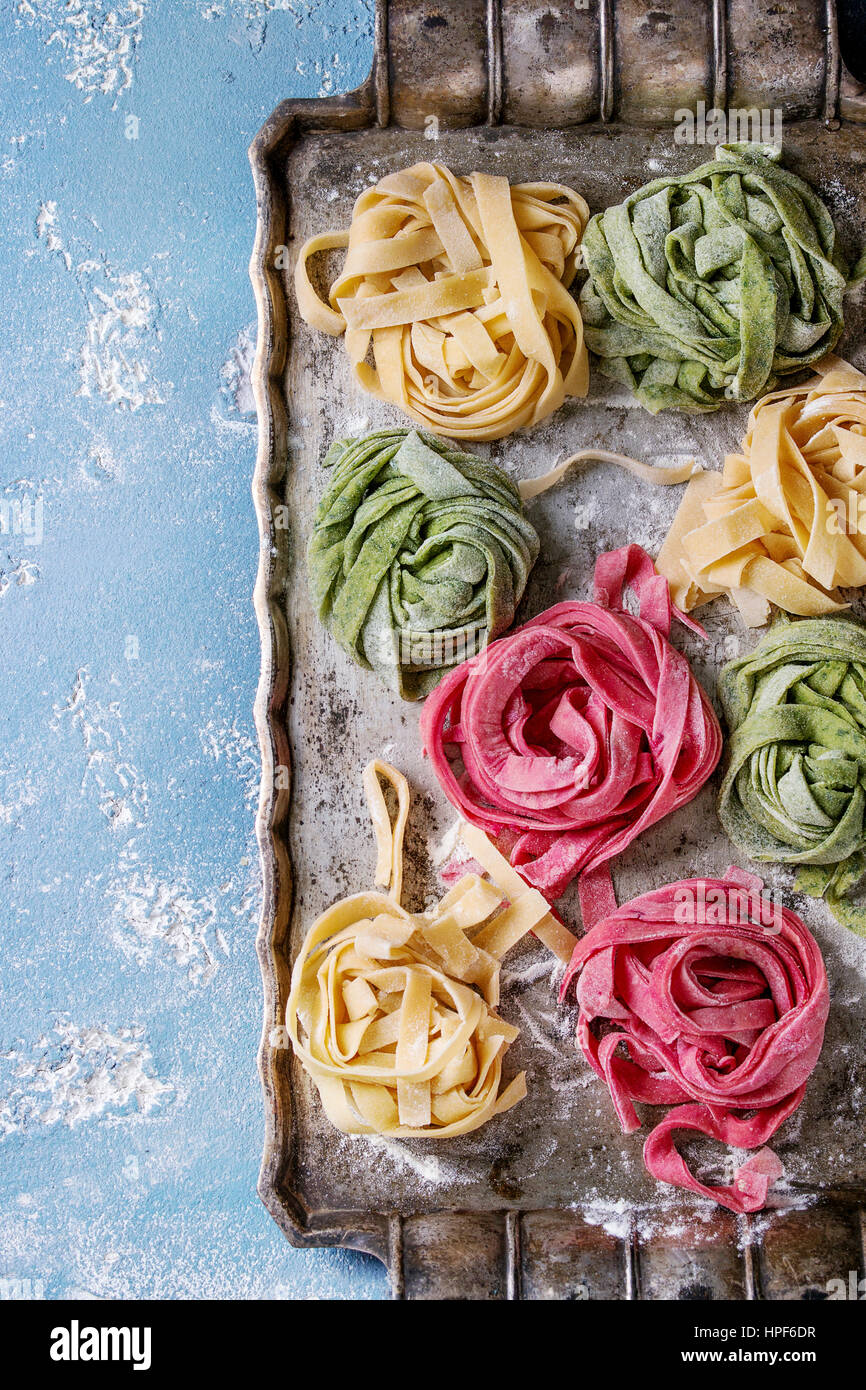 Varietà di colore crudo fresco non cotti pasta fatta in casa tagliatelle spinaci verde, rosa barbabietole rosse e gialle con farina su vecchio vassoio di metallo su blue concre Foto Stock