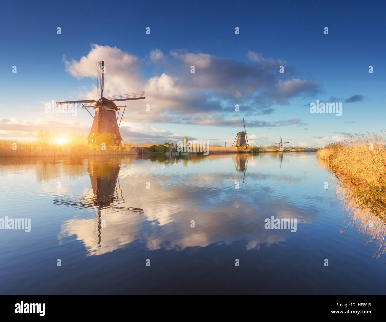 Mulini a vento di sunrise. Paesaggio agreste con sorprendente olandese di mulini a vento in prossimità dell'acqua canali con cielo blu e nuvole riflettono in acqua Foto Stock