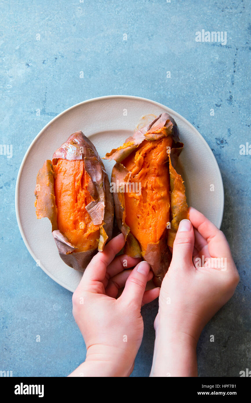 Femmina peeling delle mani appena sfornato patate dolci.vista superiore Foto Stock