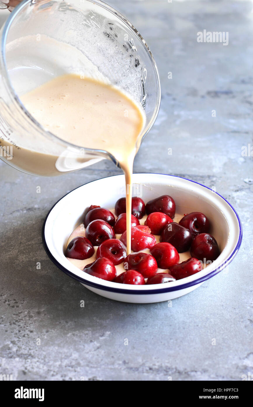 La preparazione di cherry clafoutis.Versare il composto di uova in una padella le ciliege fresche. Foto Stock