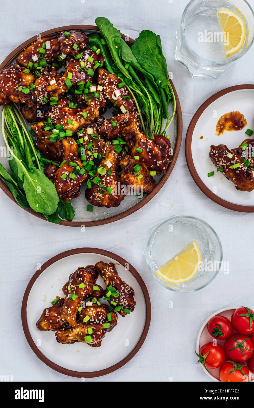 E cotte al forno ali di pollo con una salsa appiccicosa e semi di sesamo servito con erbe su una piastra grande e due piccole piastre accompagnata dalla soda con il limone Foto Stock