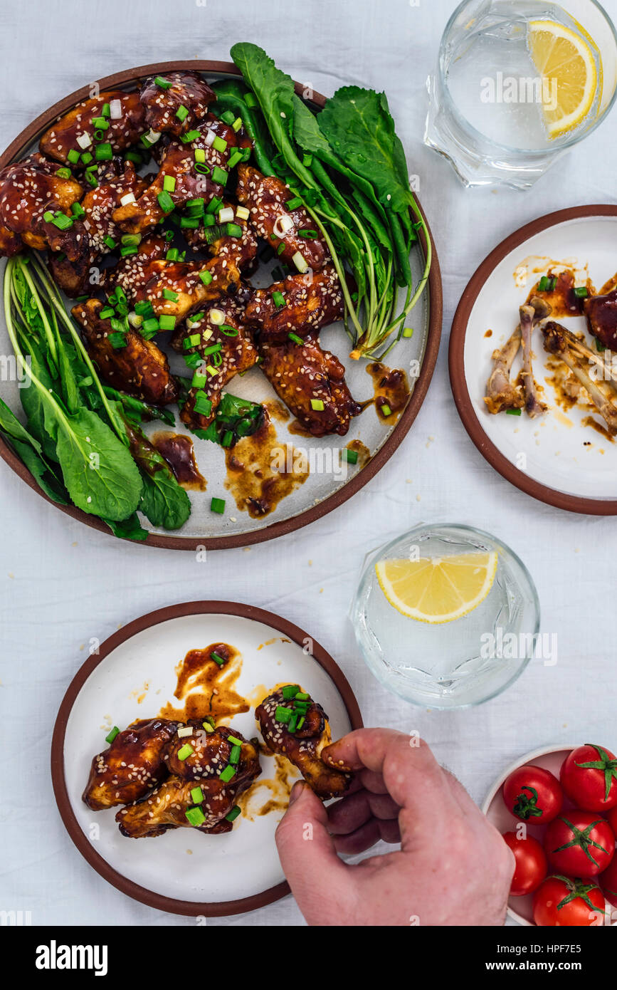 E cotte al forno ali di pollo con una salsa appiccicosa e semi di sesamo servito con erbe su una piastra grande e due piccole piastre accompagnata dalla soda con il limone Foto Stock