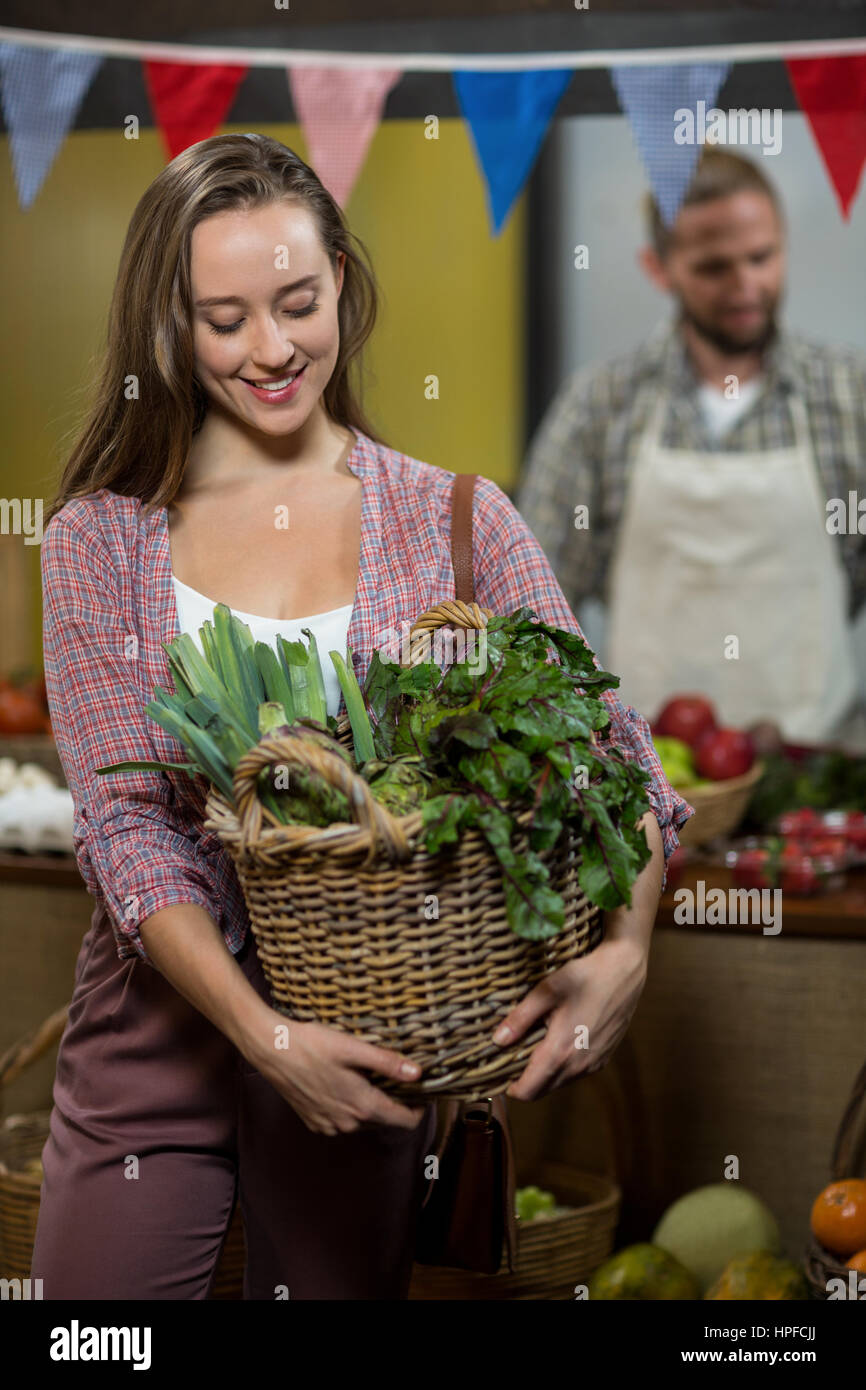 Donna sorridente cestello di contenimento di verdure a foglia verde nel negozio di alimentari Foto Stock