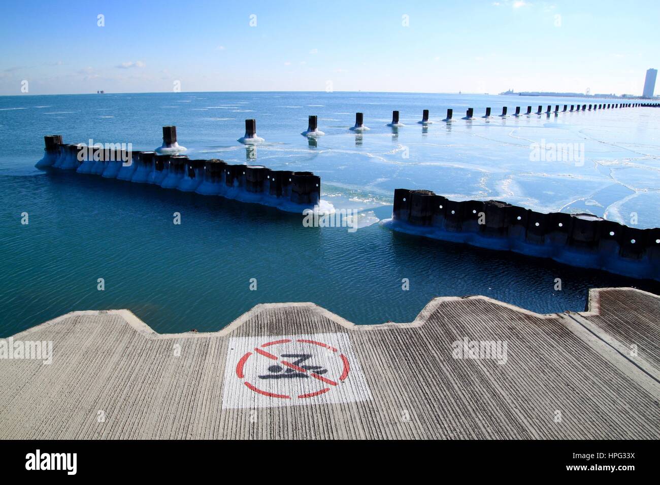 'Non nuotare' segno lungo il lago con vista di posti di legno accanto all orizzonte e sullo skyline di Chicago in un gelido lago Michigan in inverno Foto Stock