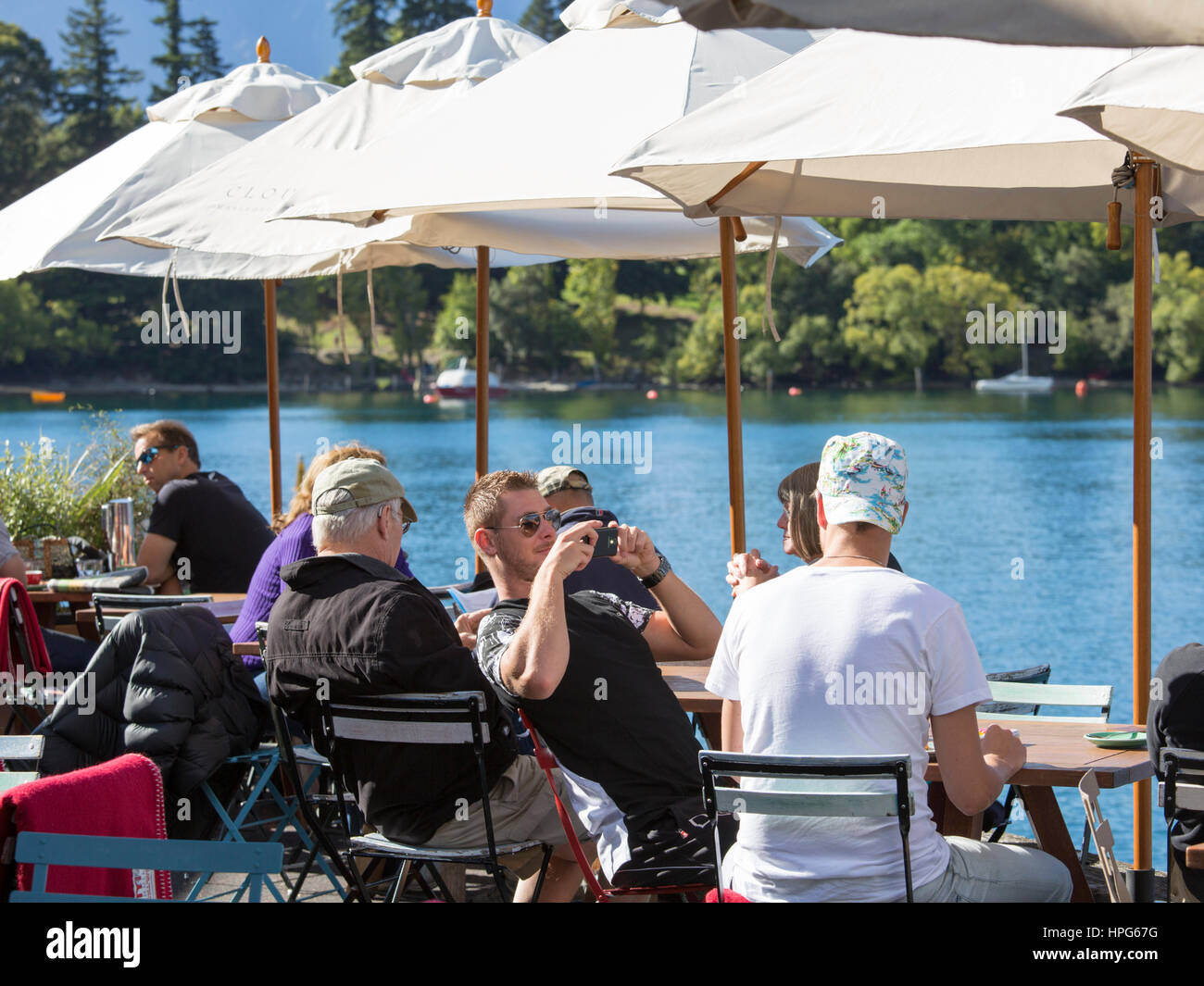 Queenstown, Otago, Nuova Zelanda. I clienti sulla terrazza di un caffè di fronte al lago, Queenstown Bay. Foto Stock