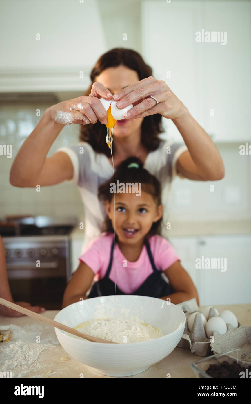 Madre e figlia la rottura delle uova nel recipiente durante la preparazione di cookie in cucina Foto Stock