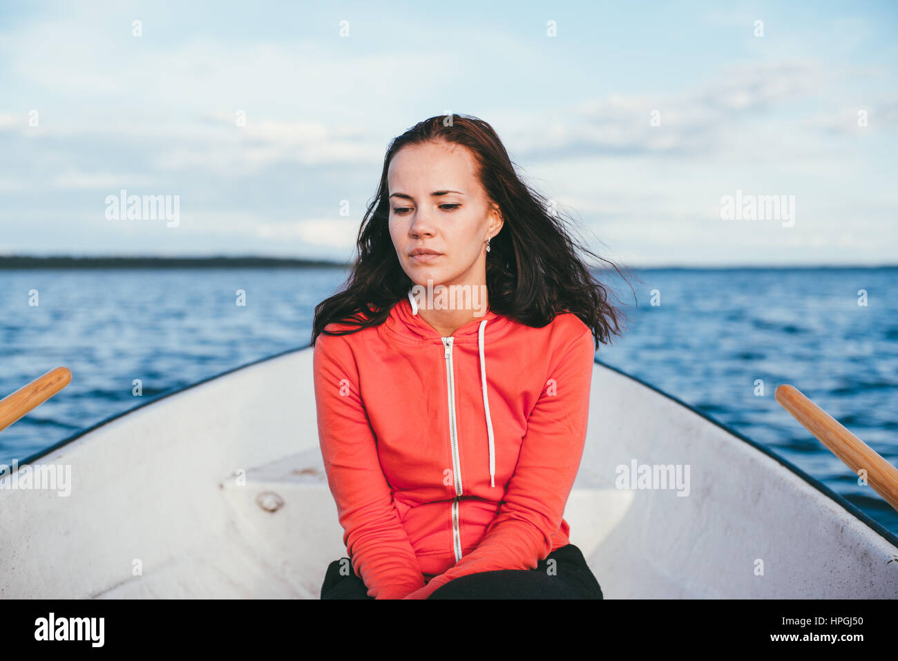 Incredibile bella ragazza dai capelli nuota su una barca di legno e canottaggio con remi in uno splendido lago di primavera. Stile di vita senza trucco. Foto Stock