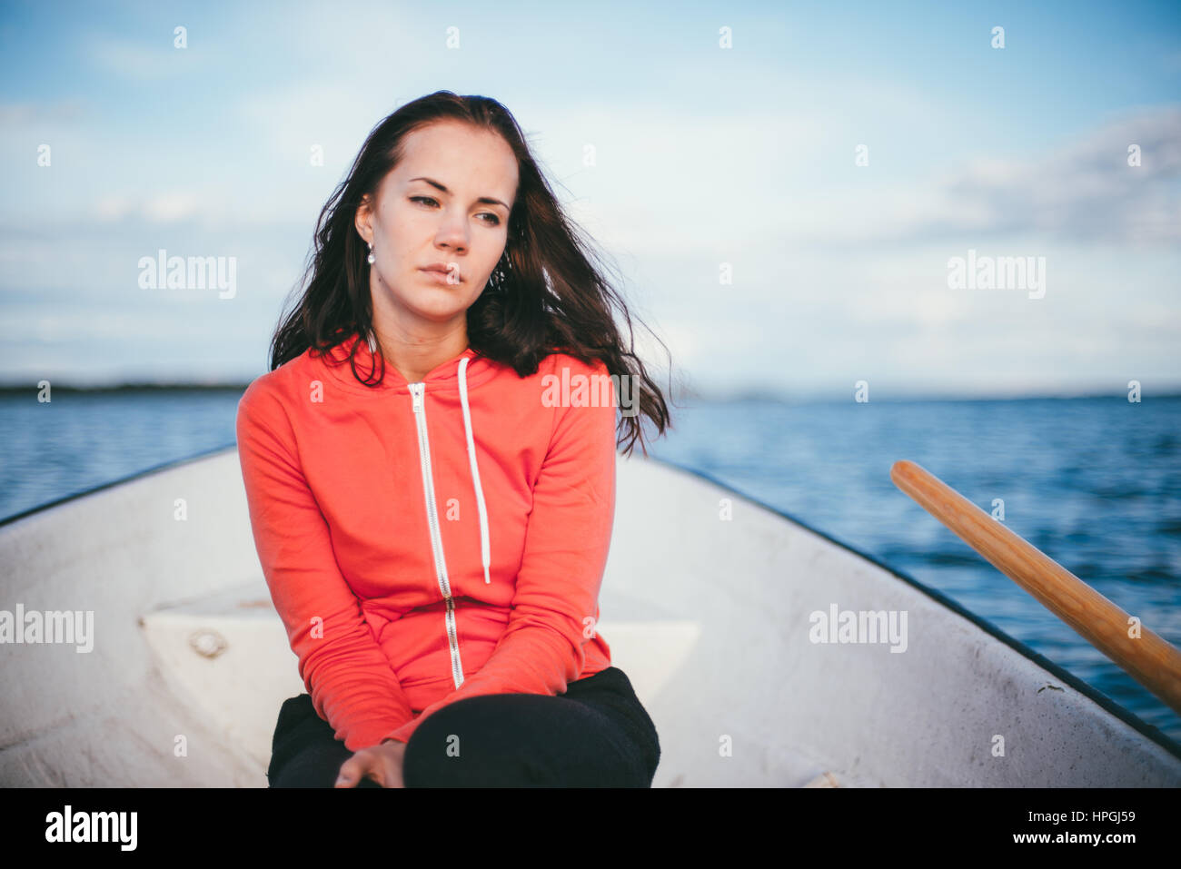 Incredibile bella ragazza dai capelli nuota su una barca di legno e canottaggio con remi in uno splendido lago di primavera. Stile di vita senza trucco. Foto Stock