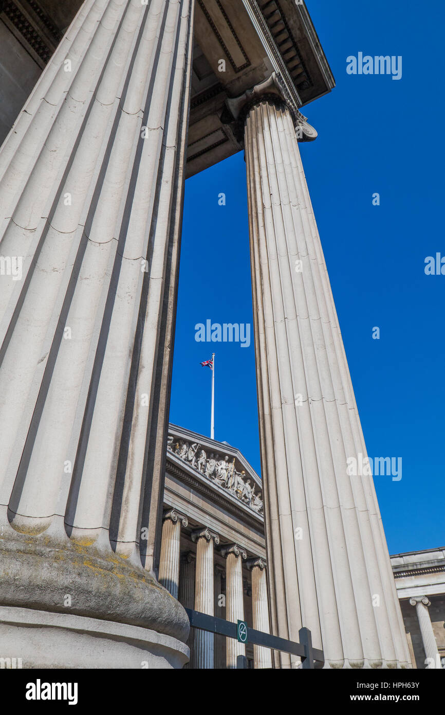 Due enormi romano colonne stlyled contro il cielo blu chiaro e un palo con un regno unito bandiera Foto Stock