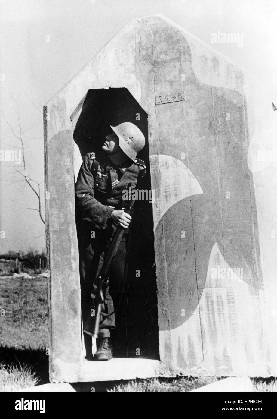 L'immagine della propaganda nazista mostra una sentinella tedesca di Wehrmacht in una casa di guardia. Pubblicato nel giugno 1944. Un reporter nazista ha scritto sul retro della foto su 02.06.1944' il nuovo sentry box. La cassa di sentry, che un tempo era fatta di legno, è ora costruita da un calcestruzzo protettivo arredato con mimetizzazione. Lo sguardo è pronto per il dovere di osservazione. Quando gli aerei nemici attaccano e le bombe cadono, può ritirarsi nella protezione all'interno della scatola di sentry." Fotoarchiv für Zeitgeschichte - NESSUN SERVIZIO WIRELESS - | utilizzo in tutto il mondo Foto Stock L'immagine della propaganda nazista mostra una sentinella tedesca di Wehrmacht in una casa di guardia. Pubblicato nel giugno 1944. Un reporter nazista ha scritto sul retro della foto su 02.06.1944' il nuovo sentry box. La cassa di sentry, che un tempo era fatta di legno, è ora costruita da un calcestruzzo protettivo arredato con mimetizzazione. Lo sguardo è pronto per il dovere di osservazione. Quando gli aerei nemici attaccano e le bombe cadono, può ritirarsi nella protezione all'interno della scatola di sentry." Fotoarchiv für Zeitgeschichte - NESSUN SERVIZIO WIRELESS - | utilizzo in tutto il mondo Foto Stock