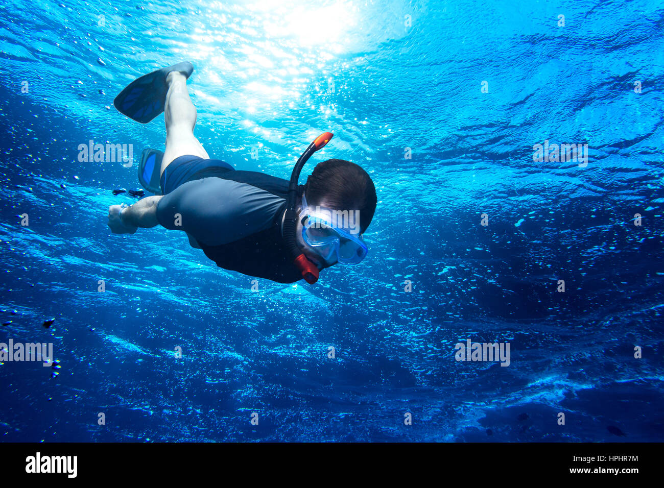 Giovane uomo immersioni subacquee Snorkeling giù nel profondo blu del mare oceano contro la luce del sole Foto Stock