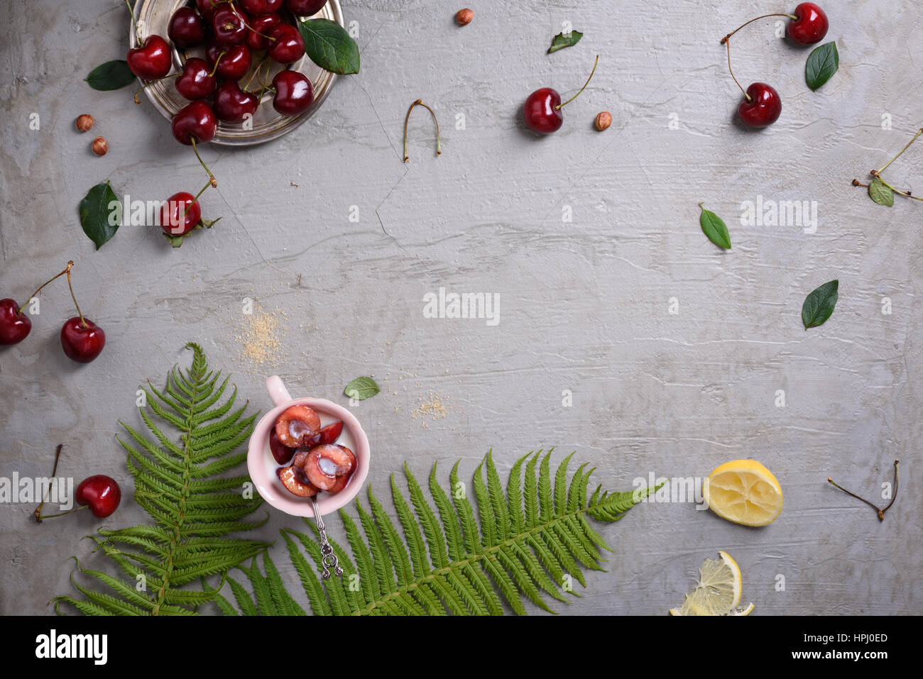 Sovraccarico di fresche ciliege rosse, clafouti dessert su superficie grigia, in stile con la felce e limone. Copia spazio, vista dall'alto. Foto Stock