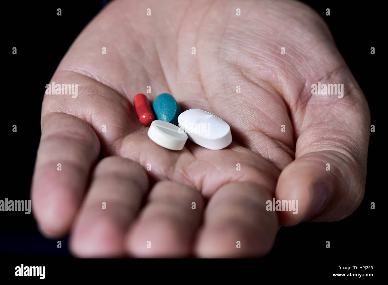 Primo piano della mano aperta di un giovane uomo caucasico con alcune diverse pillole in esso Foto Stock