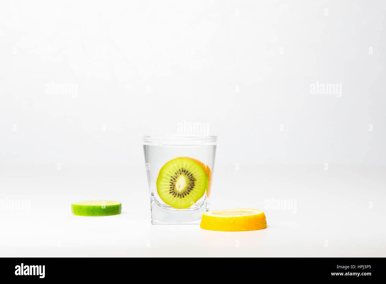 Kiwi nel bicchiere di acqua e un pezzo di limone e lime isolati su sfondo bianco Foto Stock