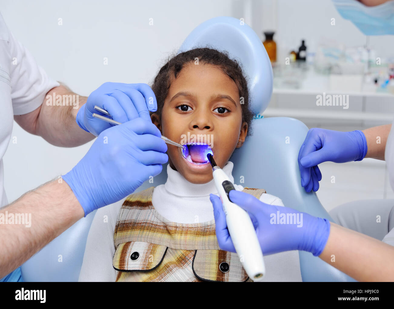Una di carnagione scura bambina sulla poltrona del dentista.dentista considera il vostro bambino i denti con una carnagione scura. La lampada UV nella bocca del paziente Foto Stock