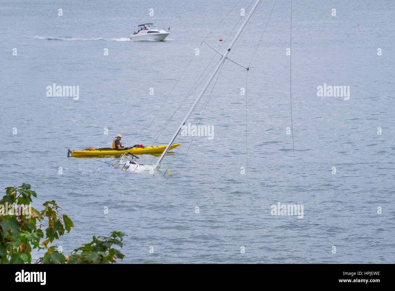 Un uomo in un giallo kayak ispeziona sommerso in barca a vela in English Bay Vancouver British Columbia Canada. Foto Stock