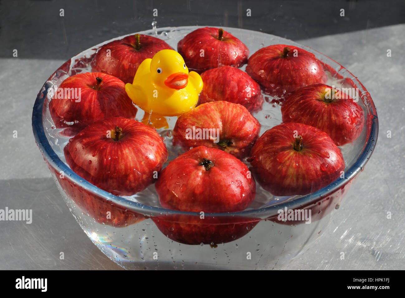 Il ducking per le mele. Giallo anatra in plastica che gode di una buona sguazzare in una ciotola di acqua e le mele rosse. Foto Stock