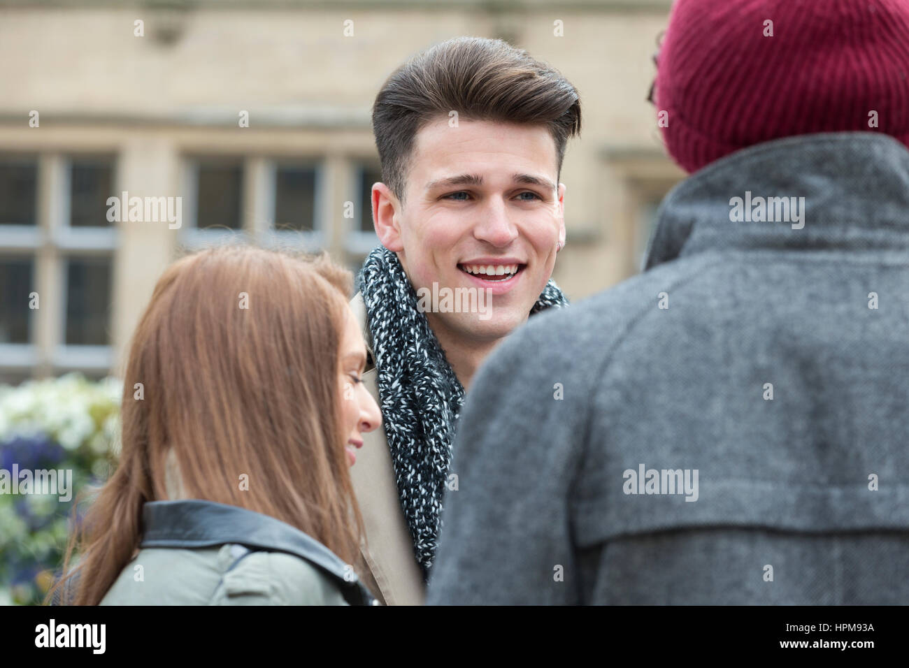 Un felice studente maschio sorrisi come egli si erge tra i suoi amici all'esterno. Essi stanno prendendo una pausa dall'università nel centro della citta'. Foto Stock