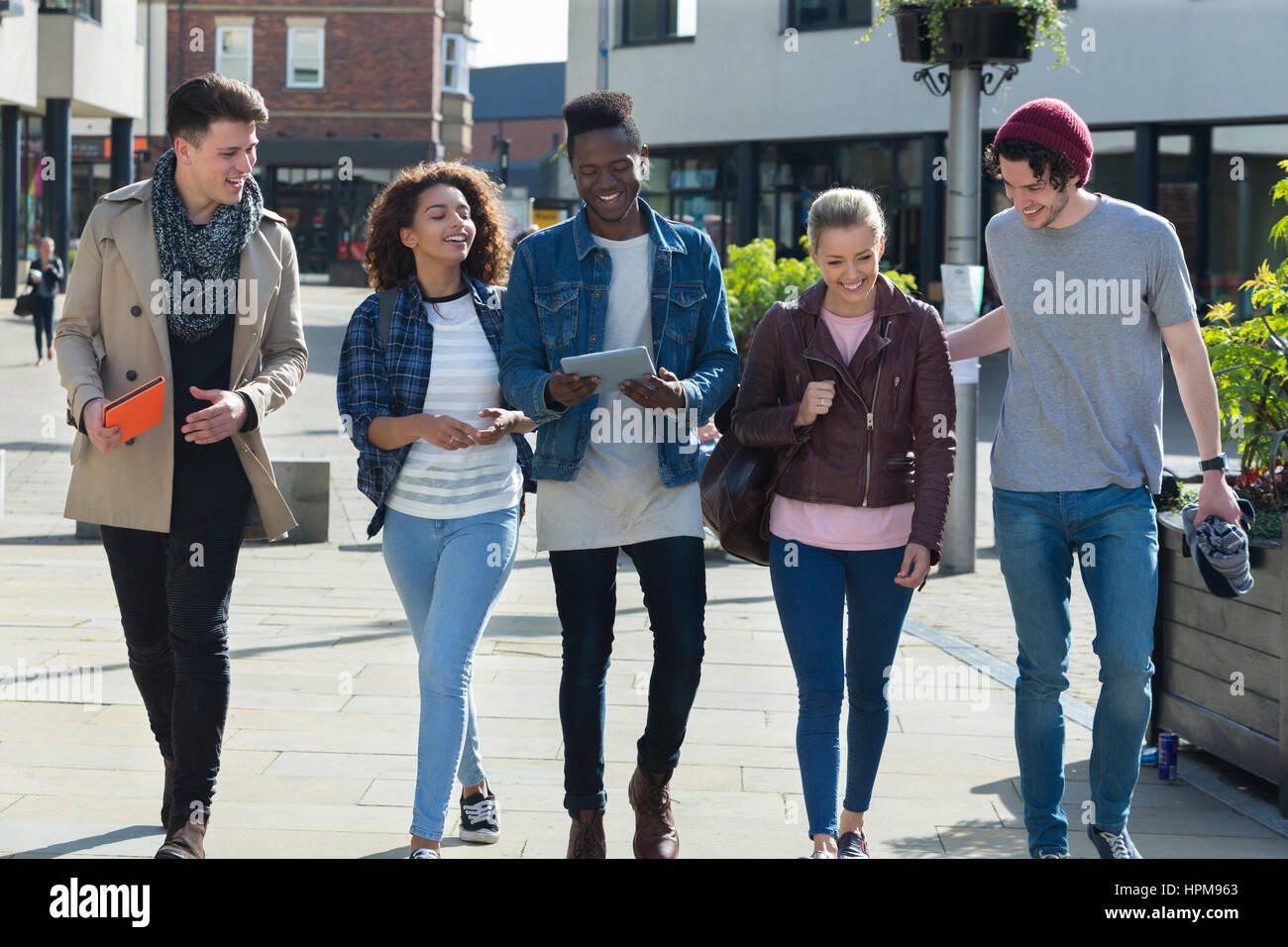 Un buon gruppo di amici sorriso a piedi attraverso la città insieme. Essi stanno portando i loro sacchi e compresse digitale su una pausa dall'università. Foto Stock