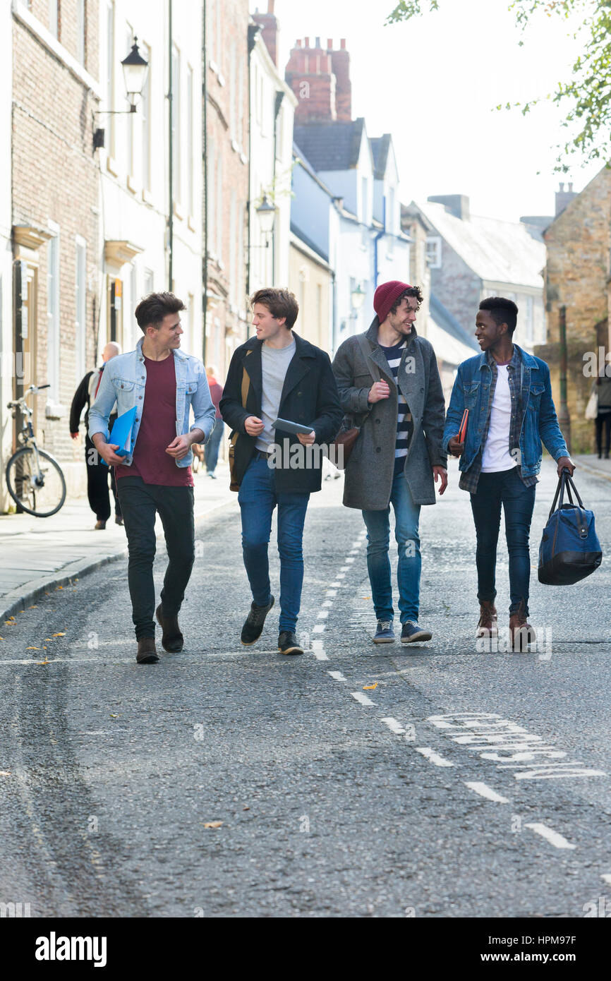 Un buon gruppo di studenti maschi sorridere e ridere come essi a piedi attraverso la città insieme. Essi stanno portando i loro sacchi e libri. Foto Stock