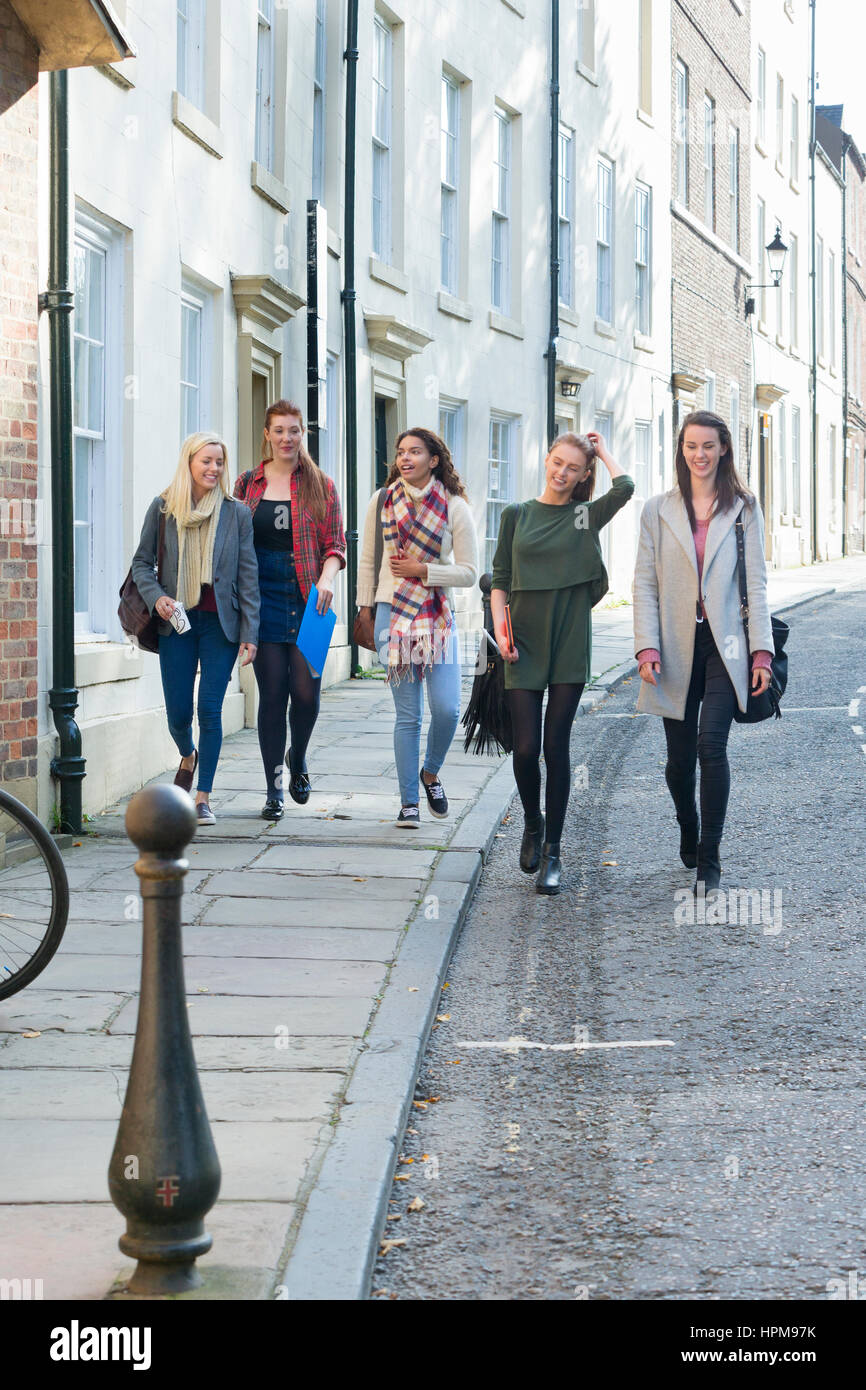 Un gruppo di giovani femmine sorriso a piedi attraverso una città insieme su una pausa dallo studio. Essi stanno portando i loro sacchi e libri lungo withe loro. Foto Stock