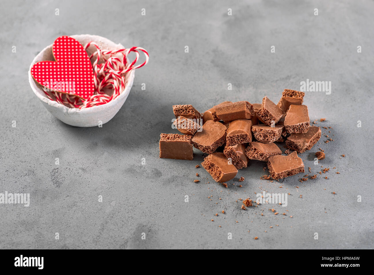 Il latte al cioccolato aerato è sul cemento grigio Sfondo. Pezzi di cioccolato sono caotica e disordinata nella composizione. Intorno alla rotta-up b al cioccolato Foto Stock