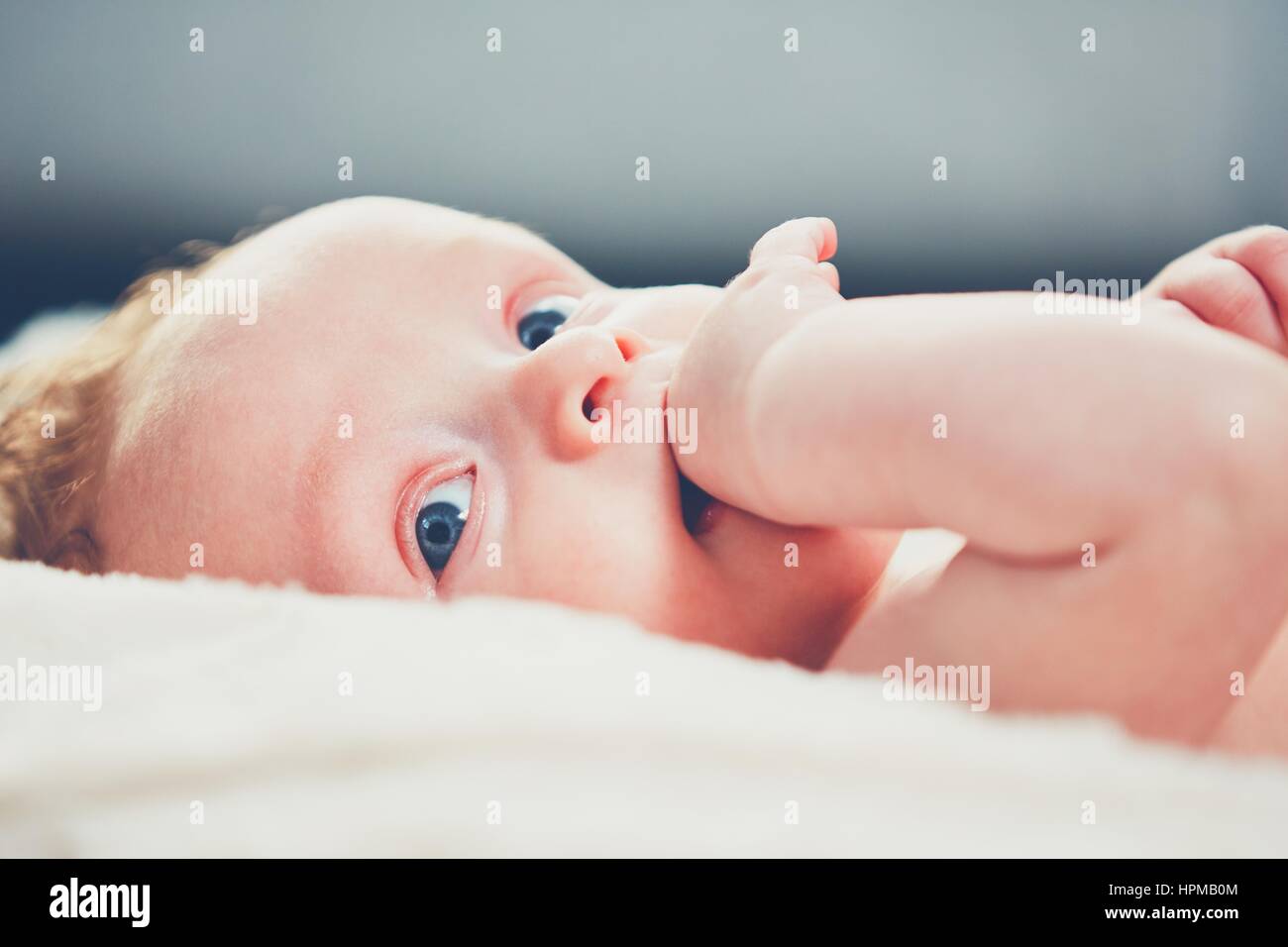 Piccolo bimbo con gli occhi blu e la mano nella sua bocca. Foto Stock