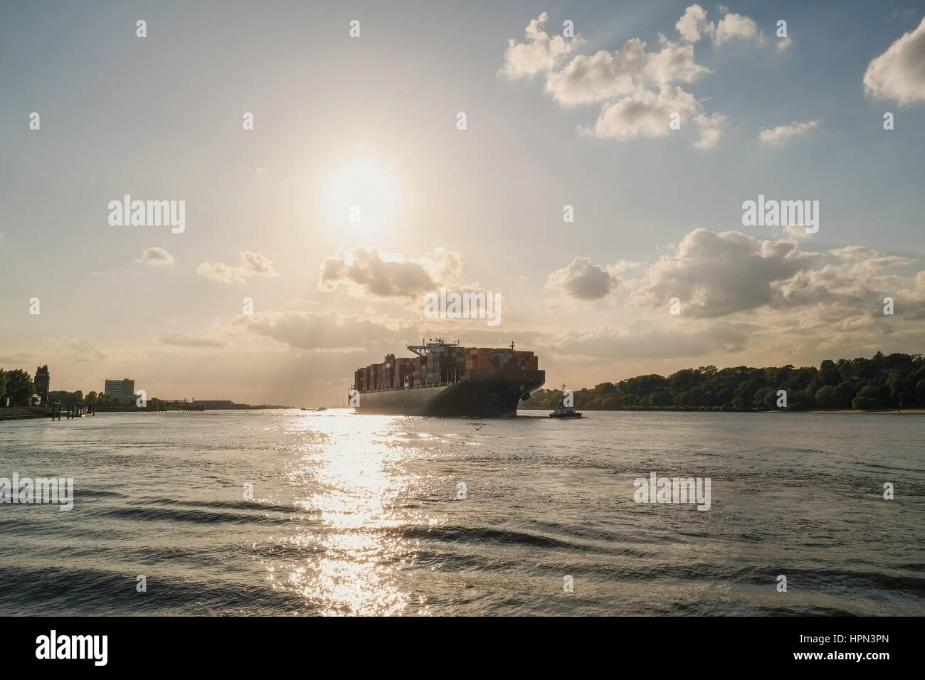 Grande nave da carico e rimorchiatore a traino su acqua in presenza di luce solare con cielo blu e nuvole di luce Foto Stock