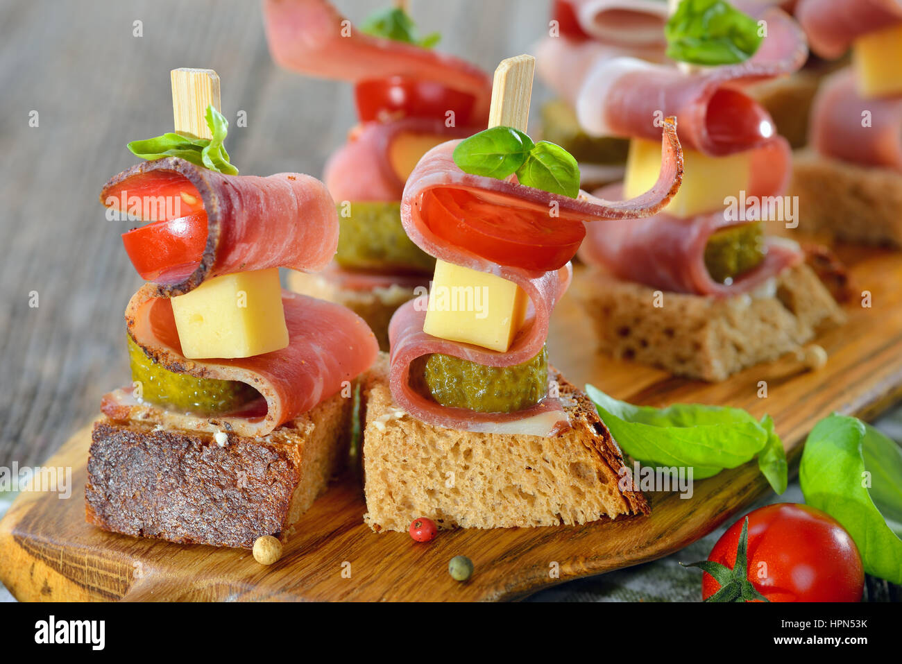 Sudtirolese antipasti: fresco imburrato pane rustico con pancetta affumicata, abbondante formaggio di montagna, sottaceti e pomodori, le foglie di basilico sulla parte superiore Foto Stock