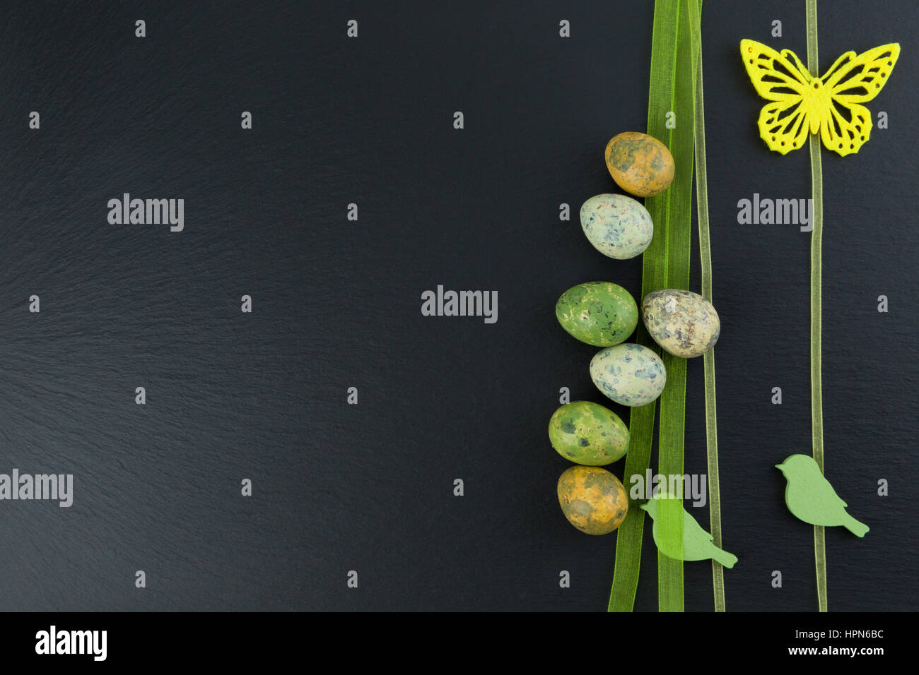 Colorate le uova di quaglia e butterfly giallo e verde uccelli di legno sul tavolo di pietra. Vista da sopra con copia spazio. Studio shot. Foto Stock