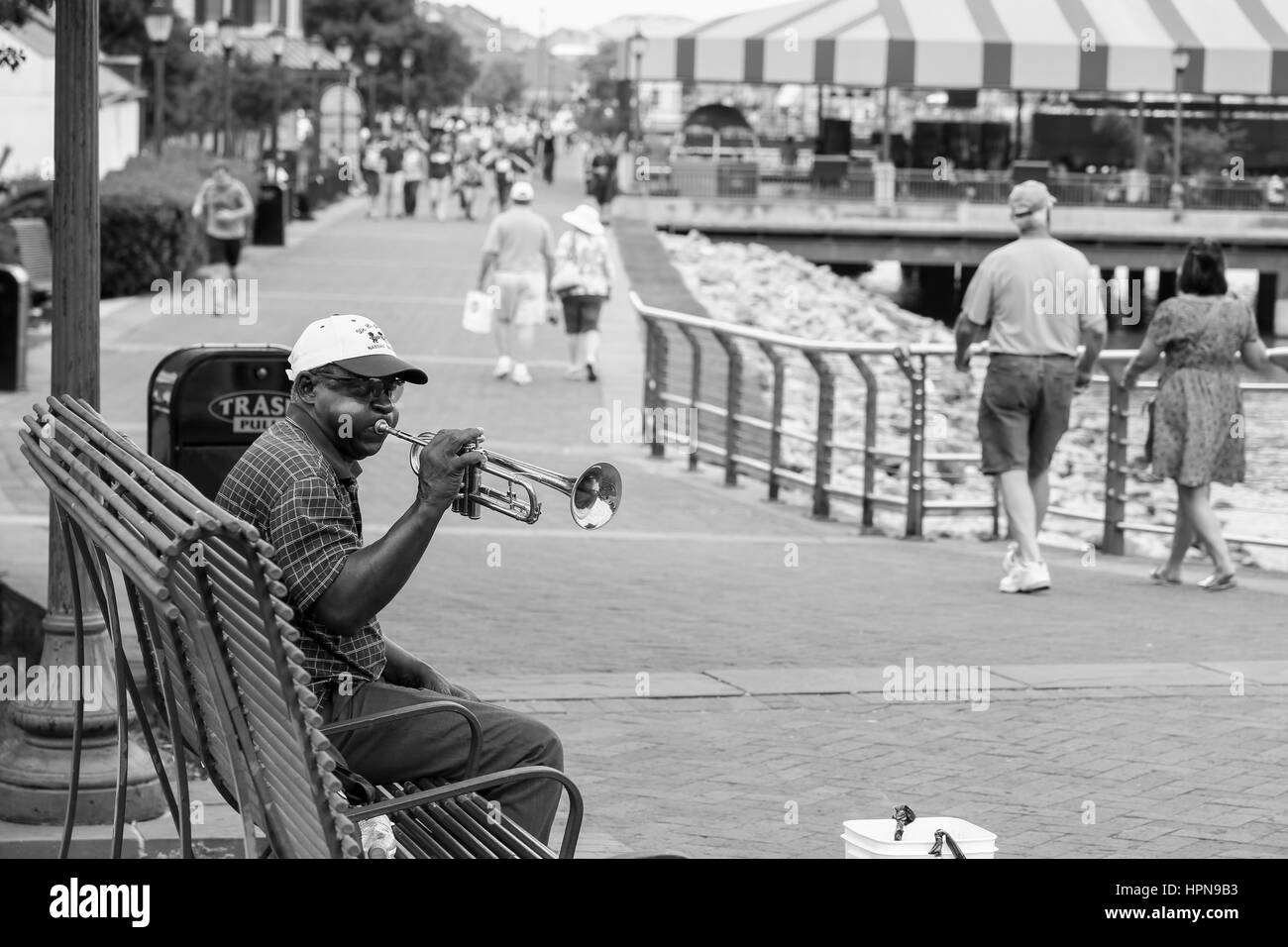 NEW ORLEANS, Stati Uniti d'America - 14 Maggio 2015: Trumpeter seduta su una panchina sul lungofiume con molte persone che camminano da. Foto Stock