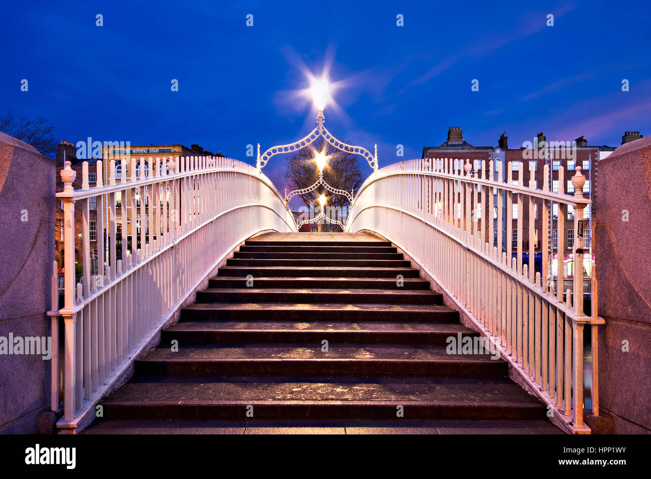 Tempo di notte vista simmetrica dei gradini che portano al Ha'penny Bridge a Dublino Irlanda.Tre lanterne illuminano il ponte. Foto Stock