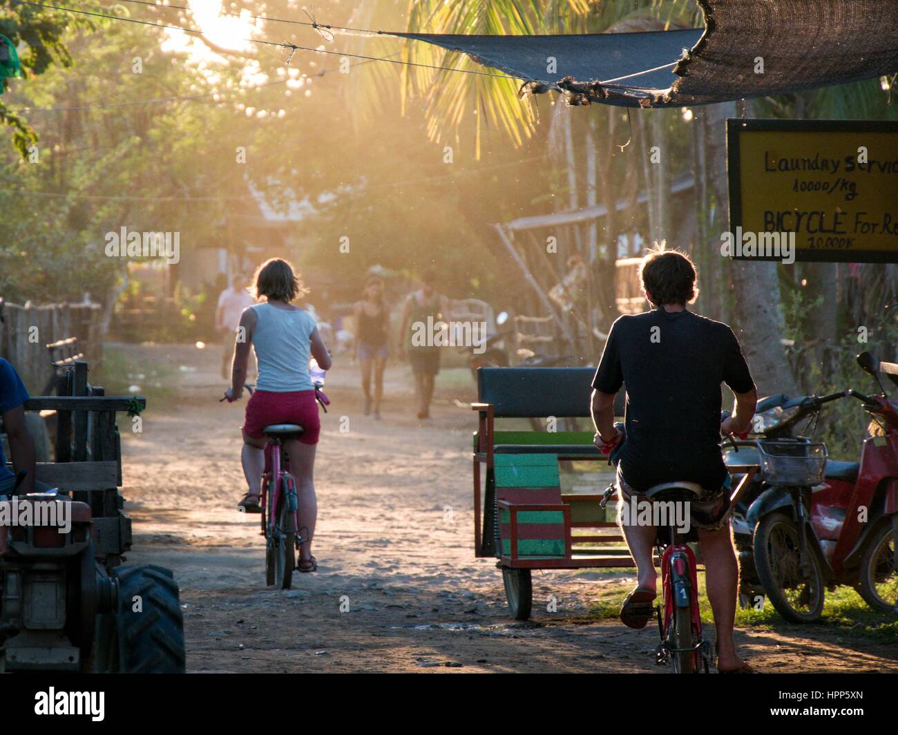 Uomo e donna Bicicletta Equitazione nella luce del tramonto sulla piccola strada asiatici street Foto Stock