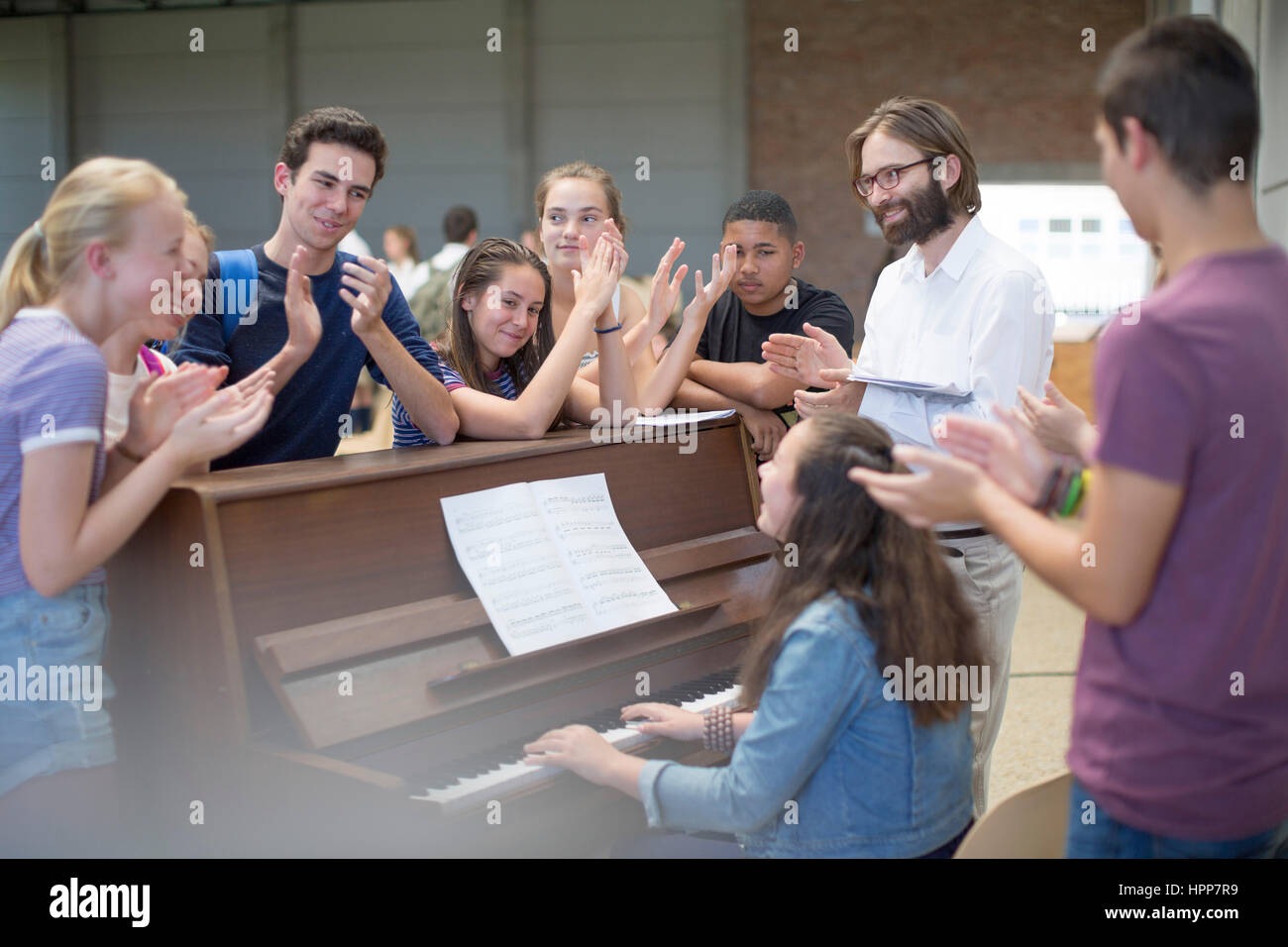 Insegnante con gruppo di studenti in piedi intorno al pianoforte e applaudire Foto Stock