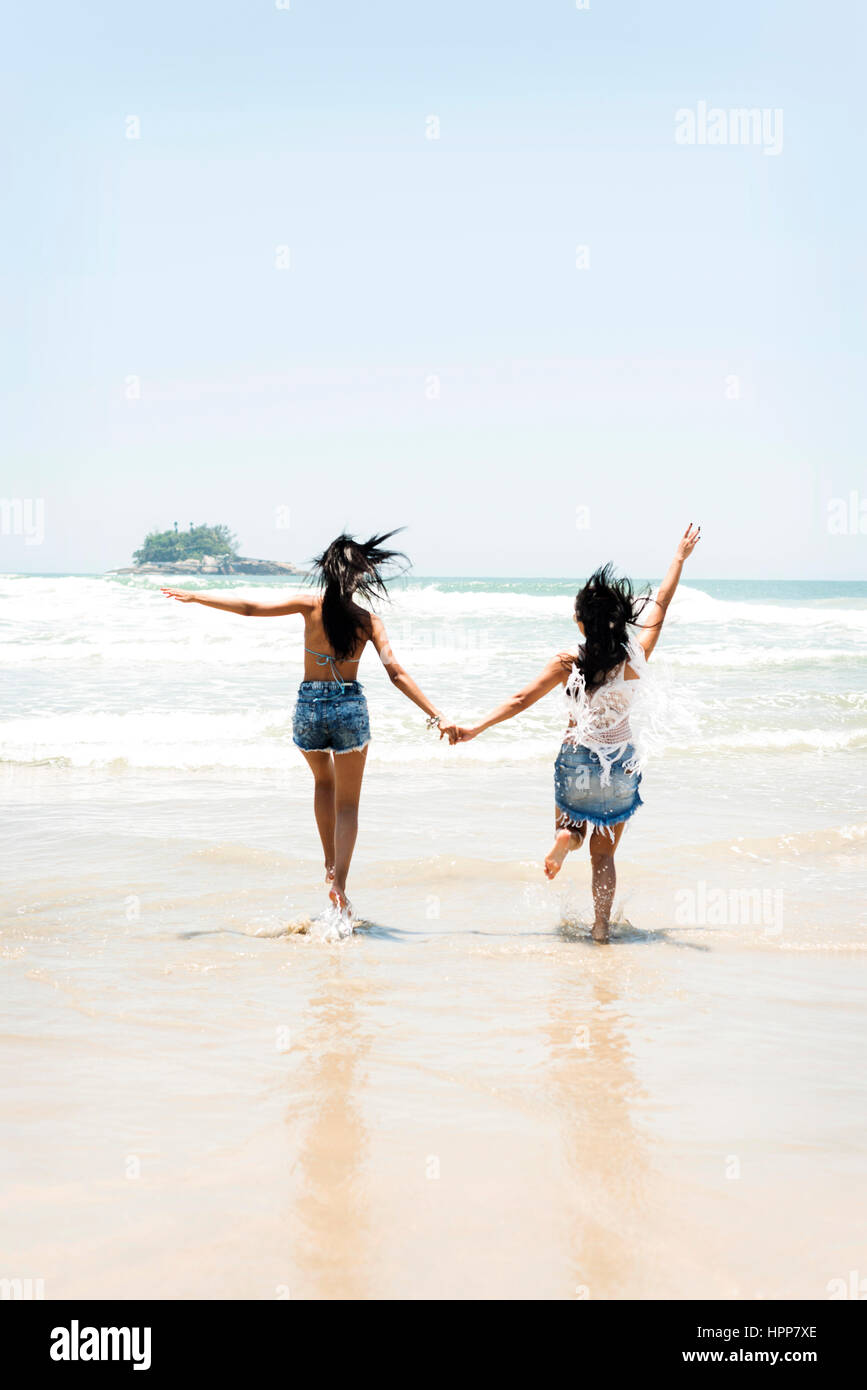 Brasil, Sao Paulo, Ubatuba, due giovani donne correre sulla spiaggia  tenendo le mani Foto stock - Alamy
