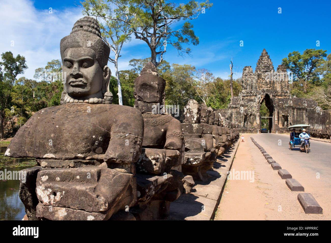 A sud o sud del cancello o Gateway di Angkor Thom con un tuk tuk passando attraverso un giorno pieno di sole con cielo blu e pietra divinità custode. Foto Stock